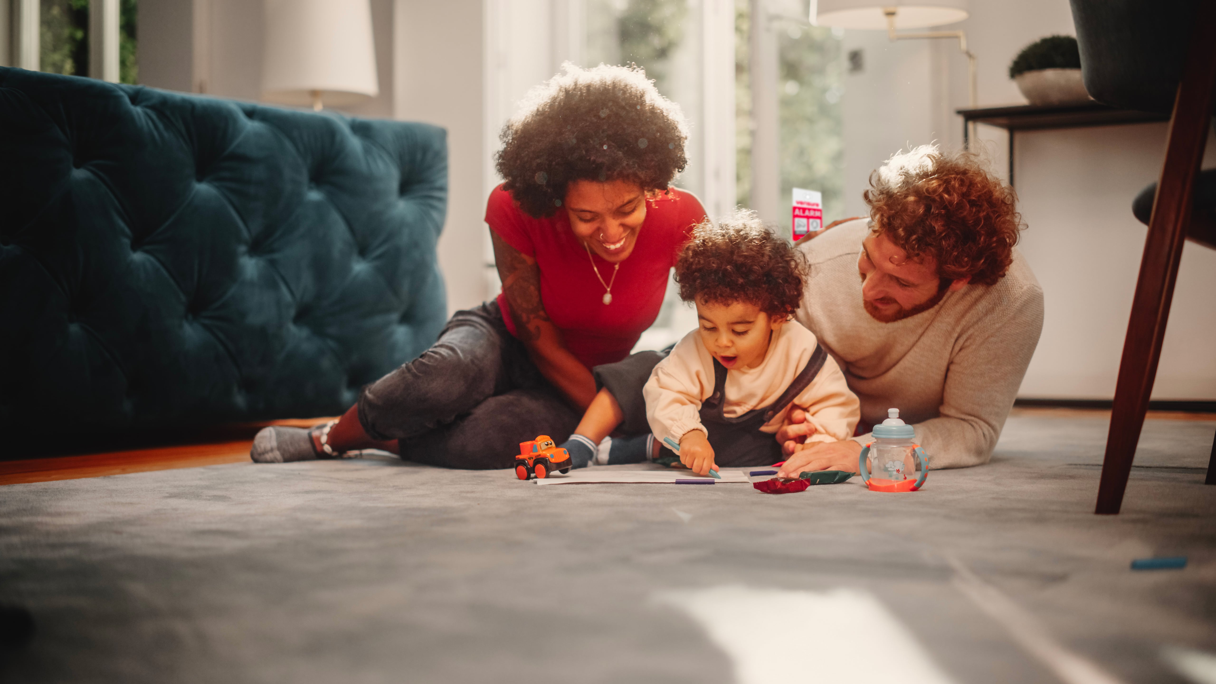 Parents with small child playing. Verisure sign in the window behind them