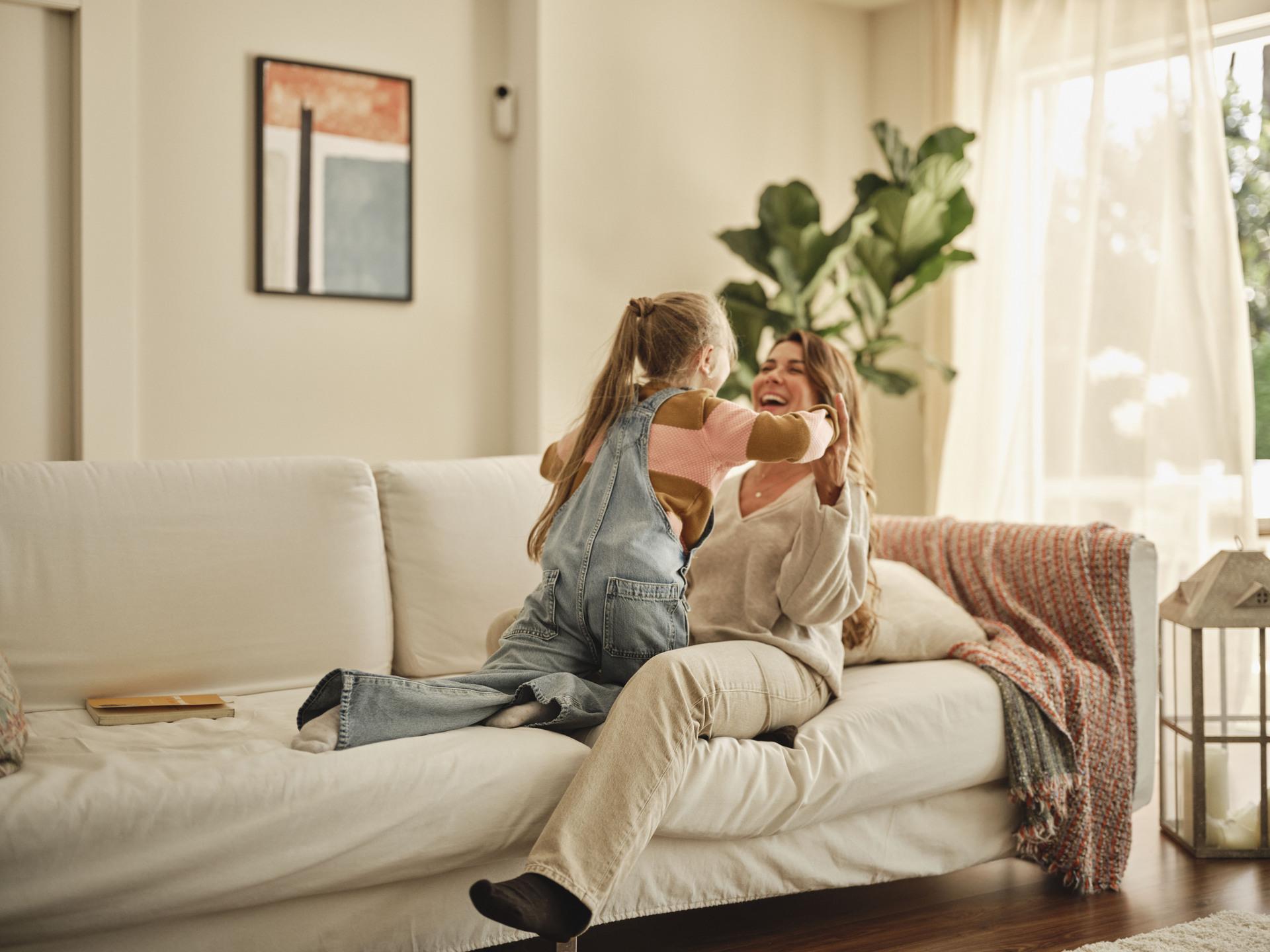 Mother and child sharing a joyful moment on a sofa at home, symbolising comfort, safety and family peace of mind.